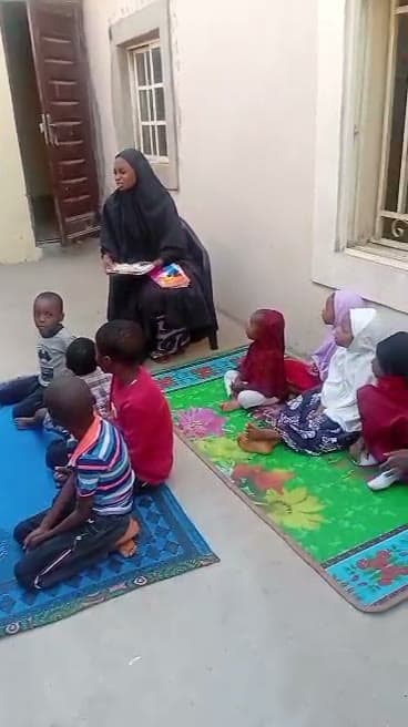 Children sitting on colourful mats around a teacher outdoors